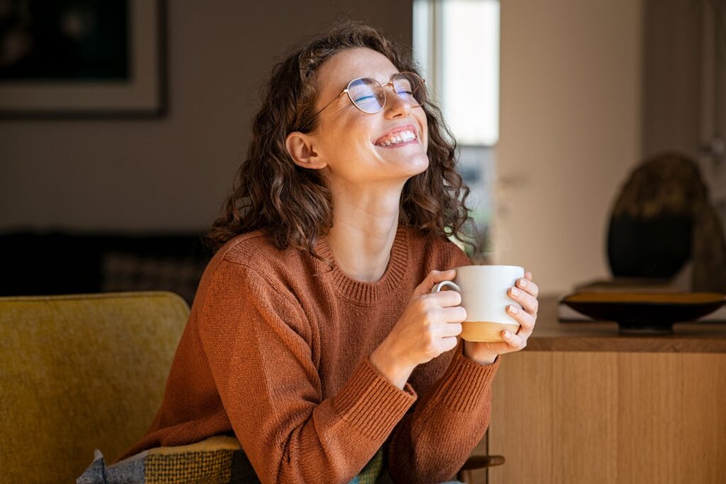 Eine Frau lächelt glücklich, während sie eine Tasse Kaffee genießt. Das Bild symbolisiert die Freude und Zufriedenheit, die ein bewusst genossener Kaffee am Morgen bringen kann.