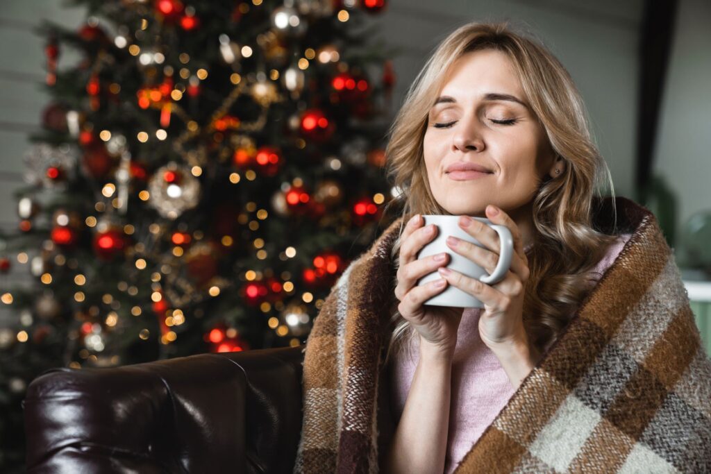 Frau entspannt mit Tee vor einem Weihnachtsbaum.