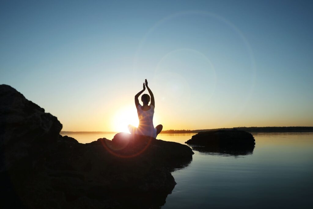 Frau macht Yoga am See bei Sonnenaufgang.